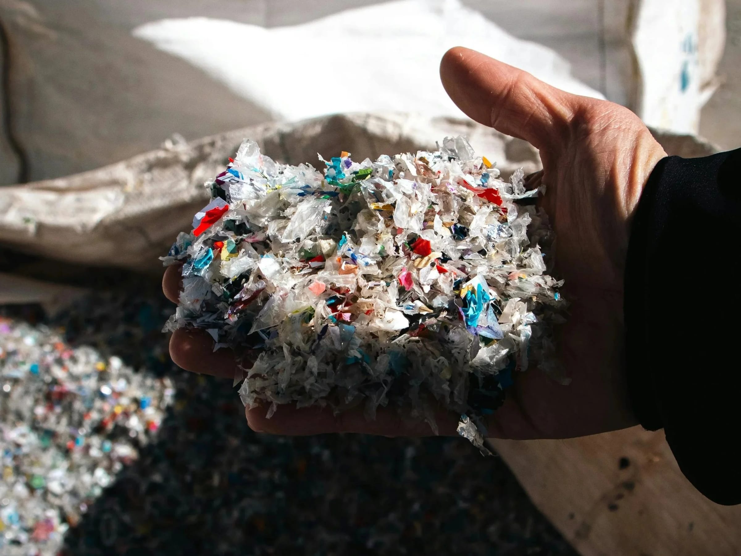 A hand holding a pile of shredded, multicolored plastic